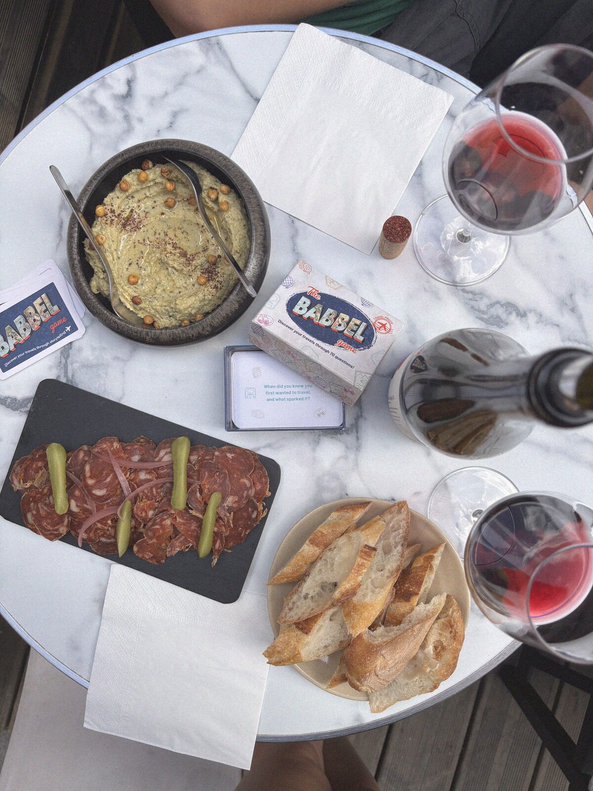 The Babbel Game box between hummus, charcuterie and red wine on a marble table